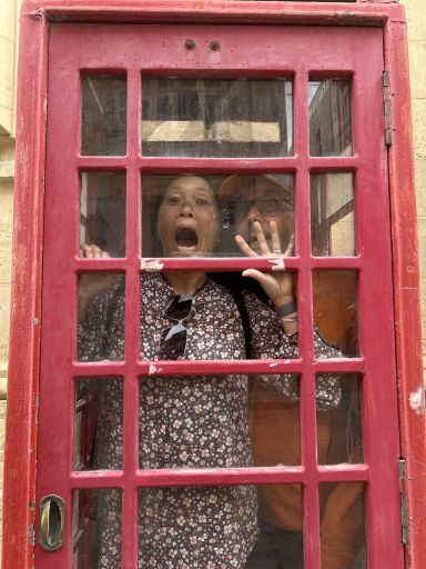 Picture of Dog and Dragon in an old red British phone booth in Malta with Dragon's mouth wide open as if she's trying to escape.